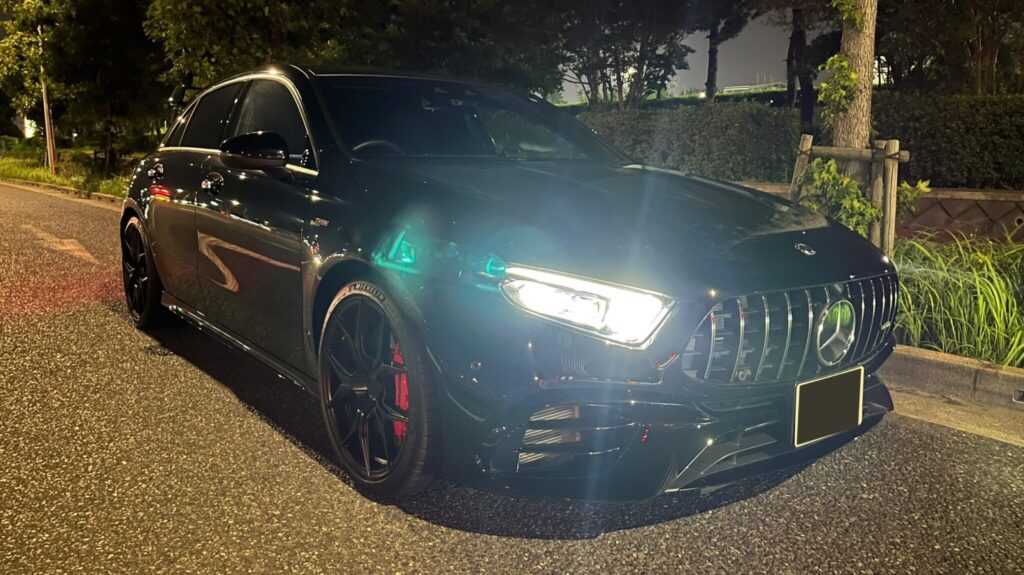 Three-quarter front view of a black Mercedes-Benz parked at night with illuminated headlights and a prominent grille.