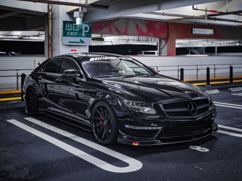 Black Mercedes-AMG sports car parked in a multi-level garage, glossy finish reflecting lights, AMG branding on windshield.