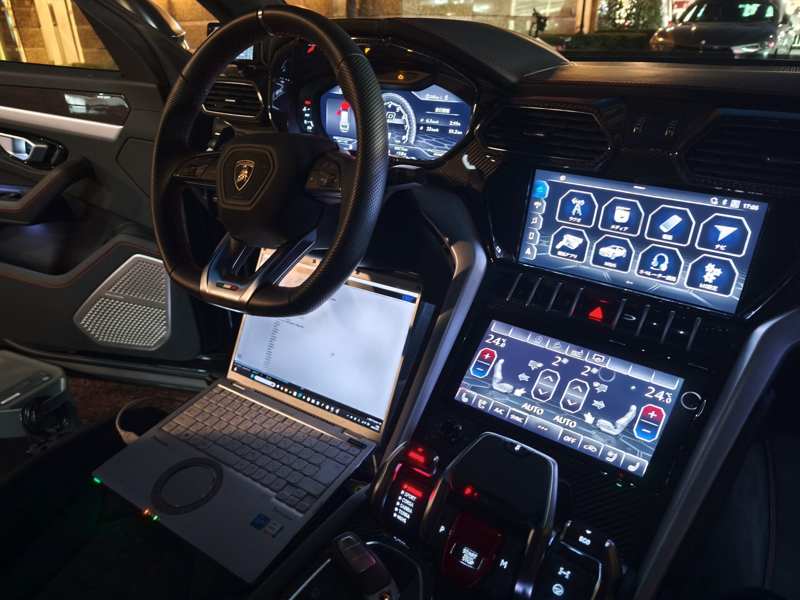 IMG_20251212_170652 – mbFAST Tuning Luxury car cockpit at night with digital instrument cluster, carbon-fiber trim, and a laptop on the passenger seat.