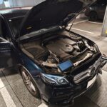 Blue Mercedes-Benz with hood open, engine visible in a parking garage.