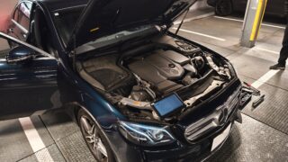 Blue Mercedes-Benz with hood open, engine visible in a parking garage.