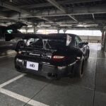 Black sports car with a large rear wing parked in a metal-floored garage.