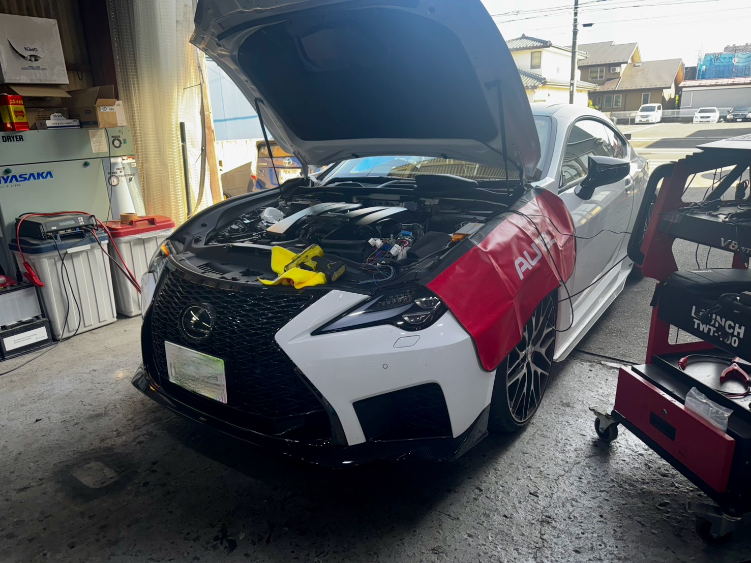 1778838507293 – mbFAST Tuning White luxury sedan in a shop with its hood up and engine exposed, tools placed over the front area, cables nearby.