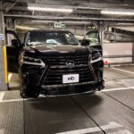 Front view of a shiny black Lexus SUV with both doors open inside an industrial parking garage on a car lift.