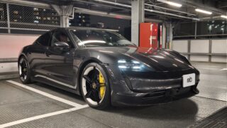 MVIMG_20260430_201251 – mbFAST Tuning Dark gray Porsche sports car parked in an industrial-looking parking garage with exposed metal beams and bright overhead lights in the background.