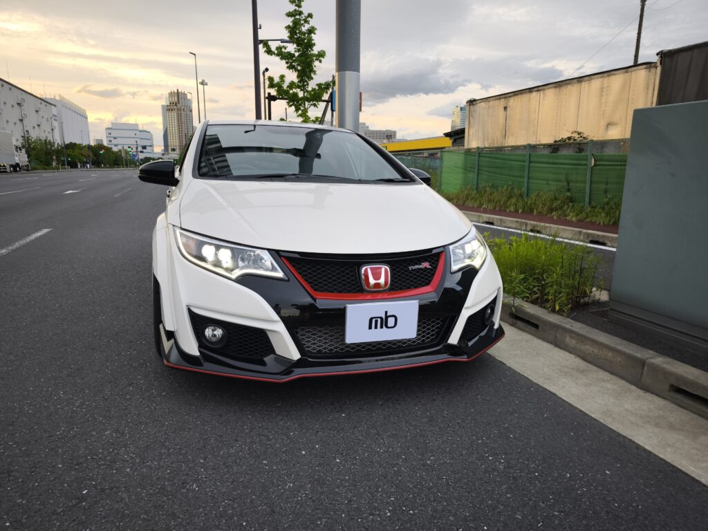 Close-up of a white Honda SUV front with red-accent grille and Type R badge, on a city street at sunset.
