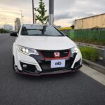 Close-up of a white Honda SUV front with red-accent grille and Type R badge, on a city street at sunset.