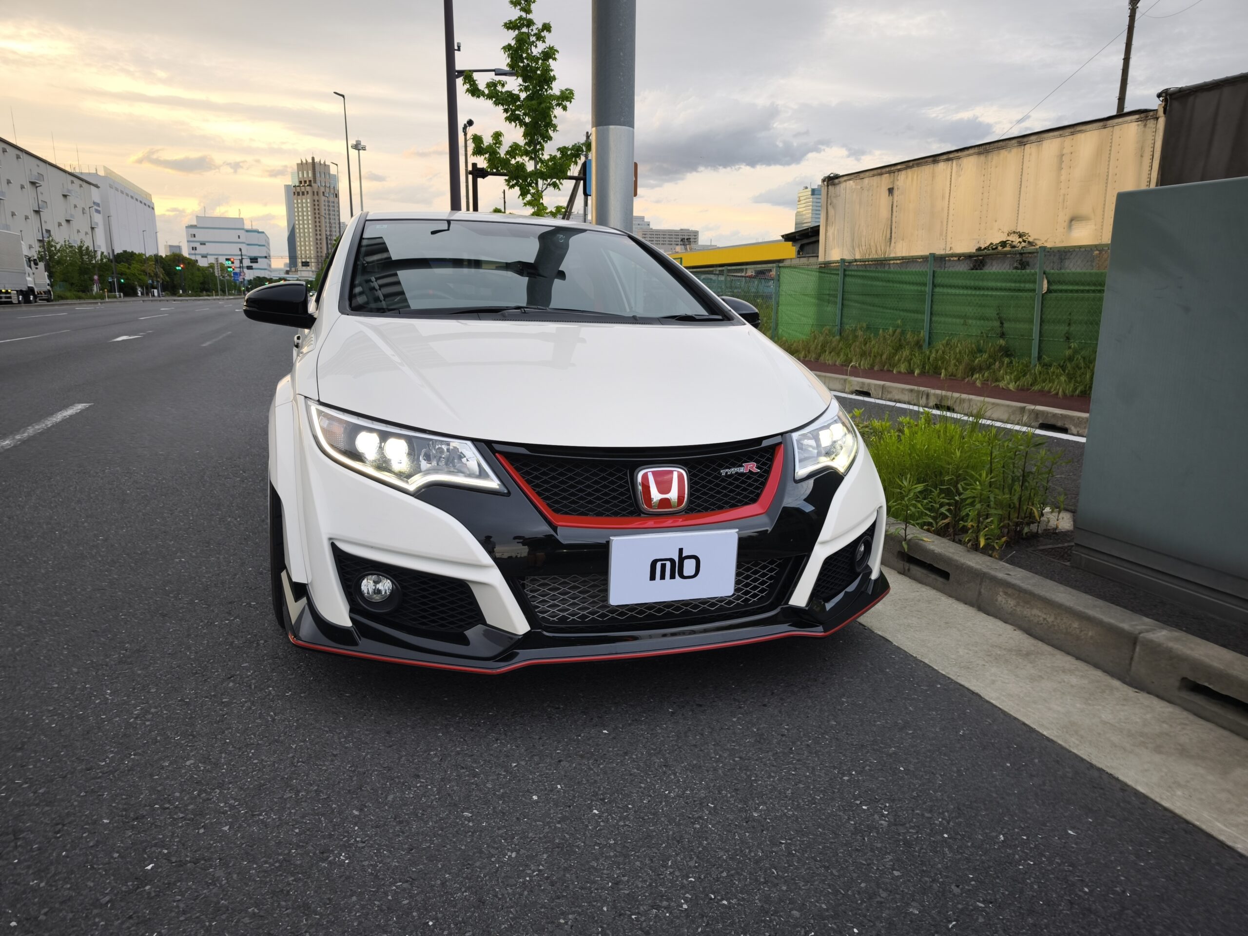 Close-up of a white Honda SUV front with red-accent grille and Type R badge, on a city street at sunset.