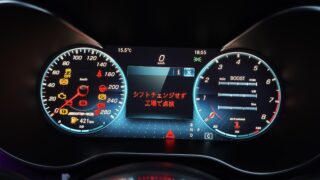 Close-up of a car's illuminated digital instrument cluster with speedometer, tachometer, and warning icons in a dark cabin.