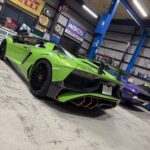 Bright green Lamborghini Aventador in a workshop with a blue car lift and tools in the background.