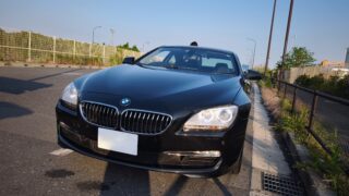 MVIMG_20260515_171236 – mbFAST Tuning Front view of a black BMW parked on a road, showing the grille and headlight with a clear blue sky above.