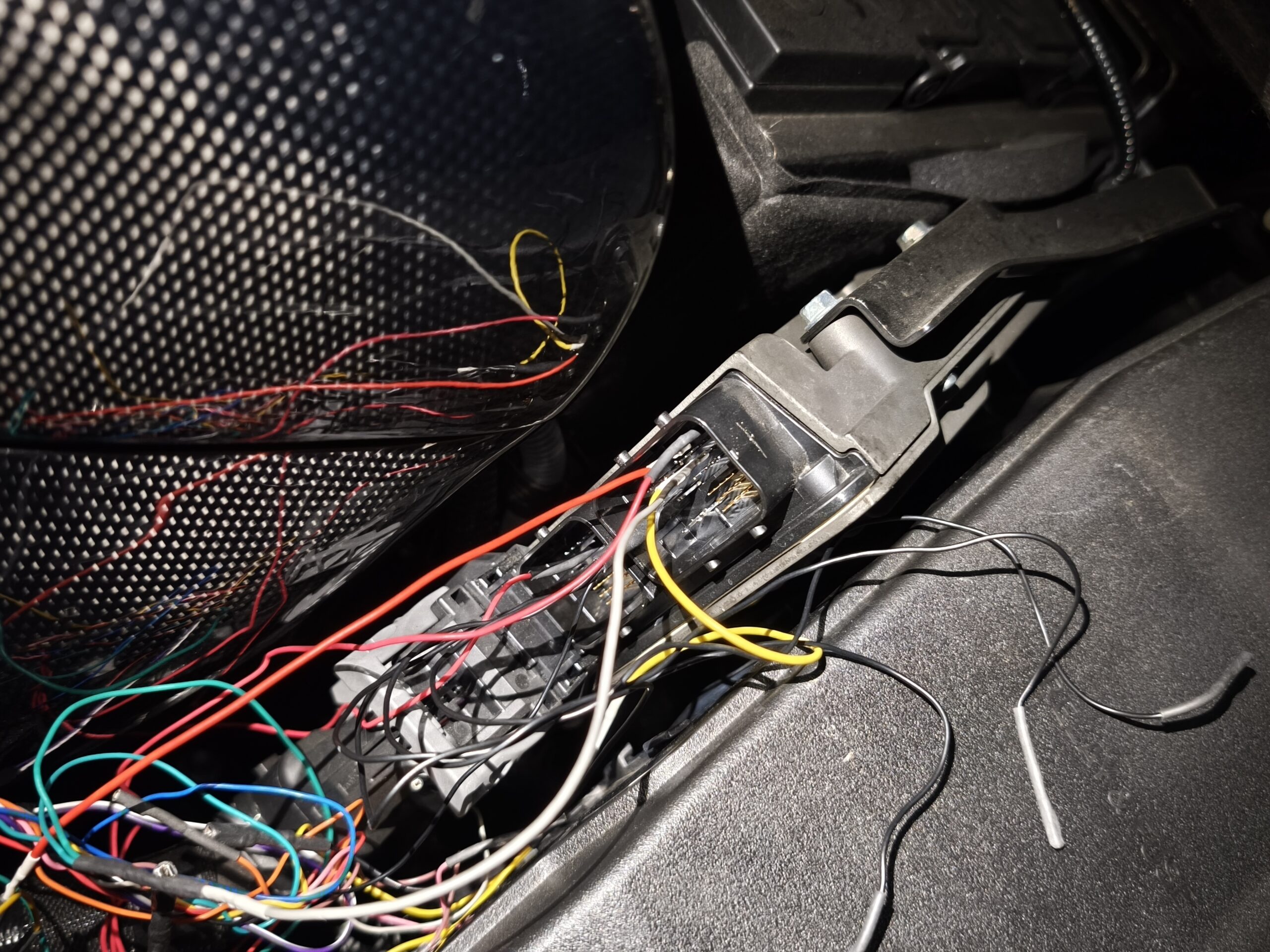 MVIMG_20260608_181633 – mbFAST Tuning Close-up of multicolored wires tangled inside a car interior near a mounting bracket and exposed connectors.