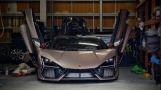 Front view of a silver Lamborghini with upward-opening doors in a cluttered garage/workshop setting
