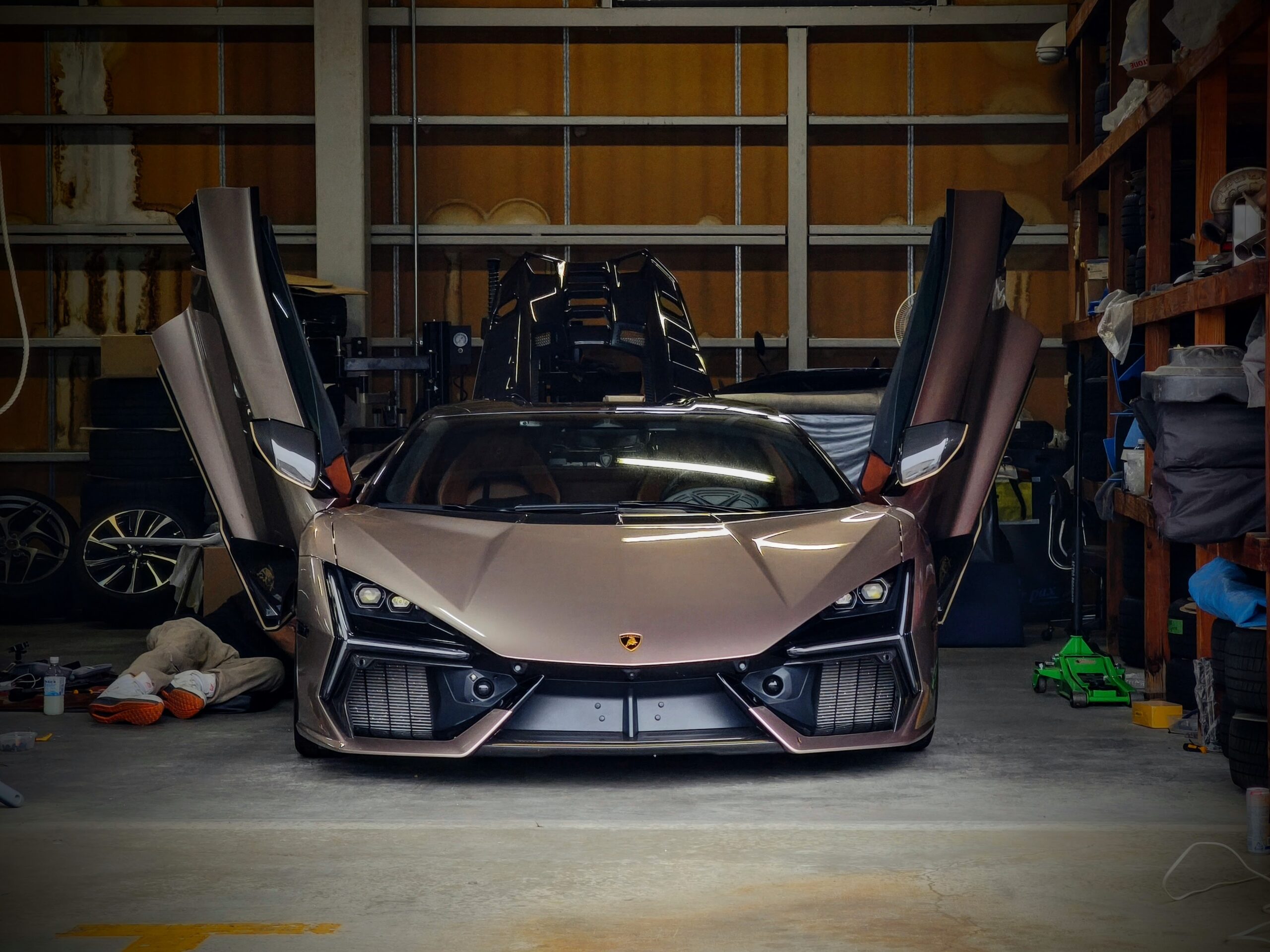 MVIMG_20260620_052853 – mbFAST Tuning Front view of a silver Lamborghini with upward-opening doors in a cluttered garage/workshop setting