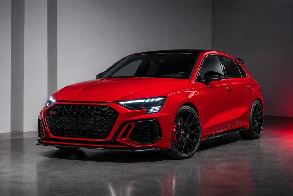 Red high-performance hatchback parked indoors with a black honeycomb grille, sharp LED headlights, and large black alloy wheels.