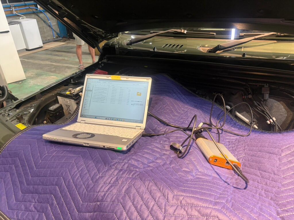 WhatsApp Image 2026-05-27 at 211800 1 – mbFAST Tuning Laptop on a purple padded mat in an open car trunk, connected to an orange diagnostic device with cables for vehicle testing in a workshop.