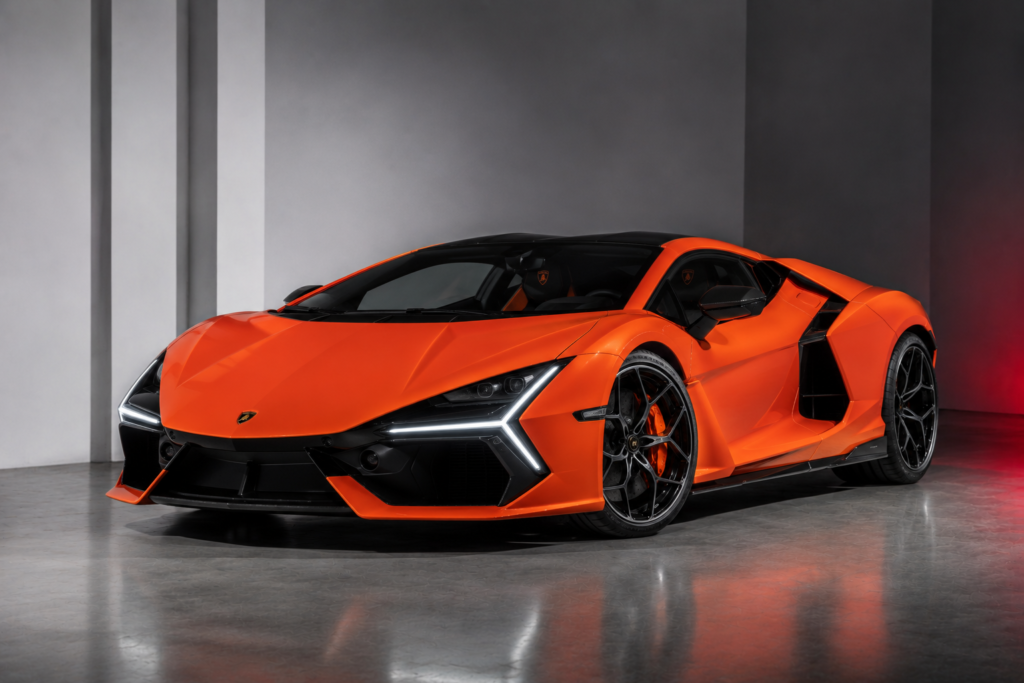 Orange Lamborghini supercar in a showroom, shown from a front-left three-quarter view with bold black accents and large alloy wheels.