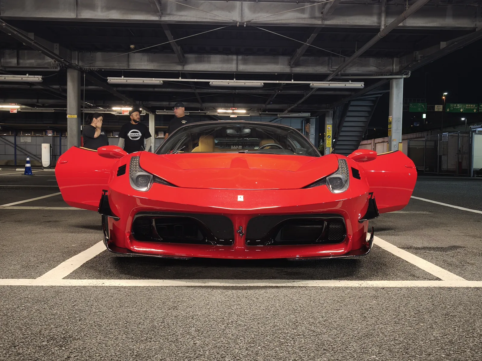 exotic-ecu-tuning-flames – mbFAST Tuning Front view of a bright red sports car with its doors open in an underground parking garage, with three people standing behind the car.