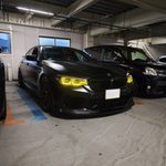 Indoor parking garage with several parked cars, including a dark BMW in the foreground and a row of vehicles in the background.