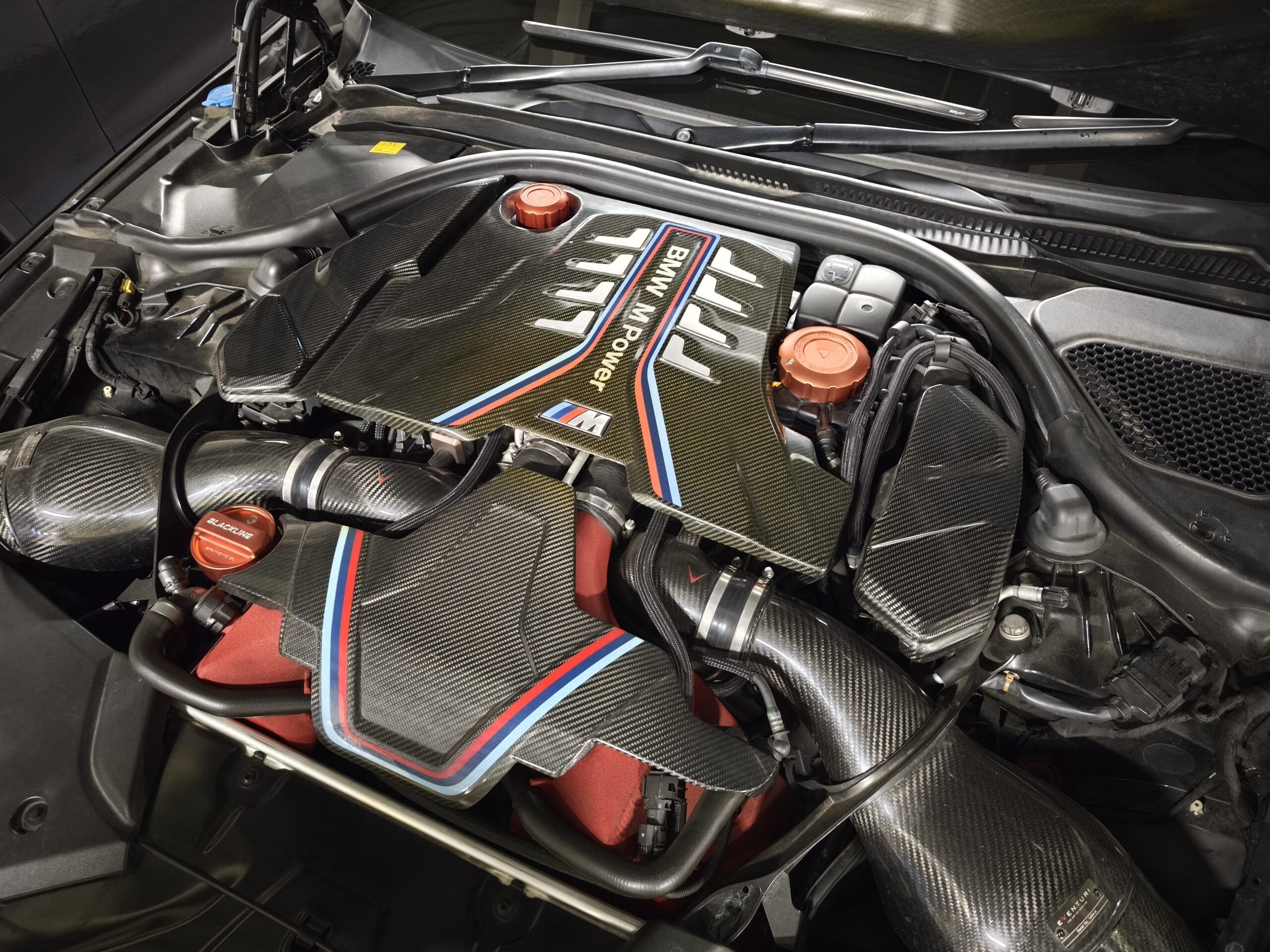 BMW F90 M5 Competitionのエンジンルーム。カーボンカバーとレッドのオイルフィラーキャップが見える