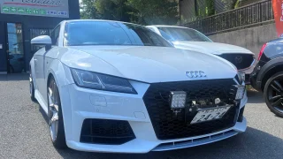 audi-tt-8s-bubbling-tuning-1 – mbFAST Tuning White Audi sports car front view with honeycomb grille and aftermarket LED light panels, Japanese license plate visible in a parking lot.