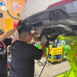 リフトアップされた車両下部でスタッフ2名がワンオフマフラーの取り付け作業を行っている様子