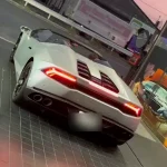 White exotic mid-engine sports car seen from the rear, with red tail lights and quad exhausts on a tiled floor.