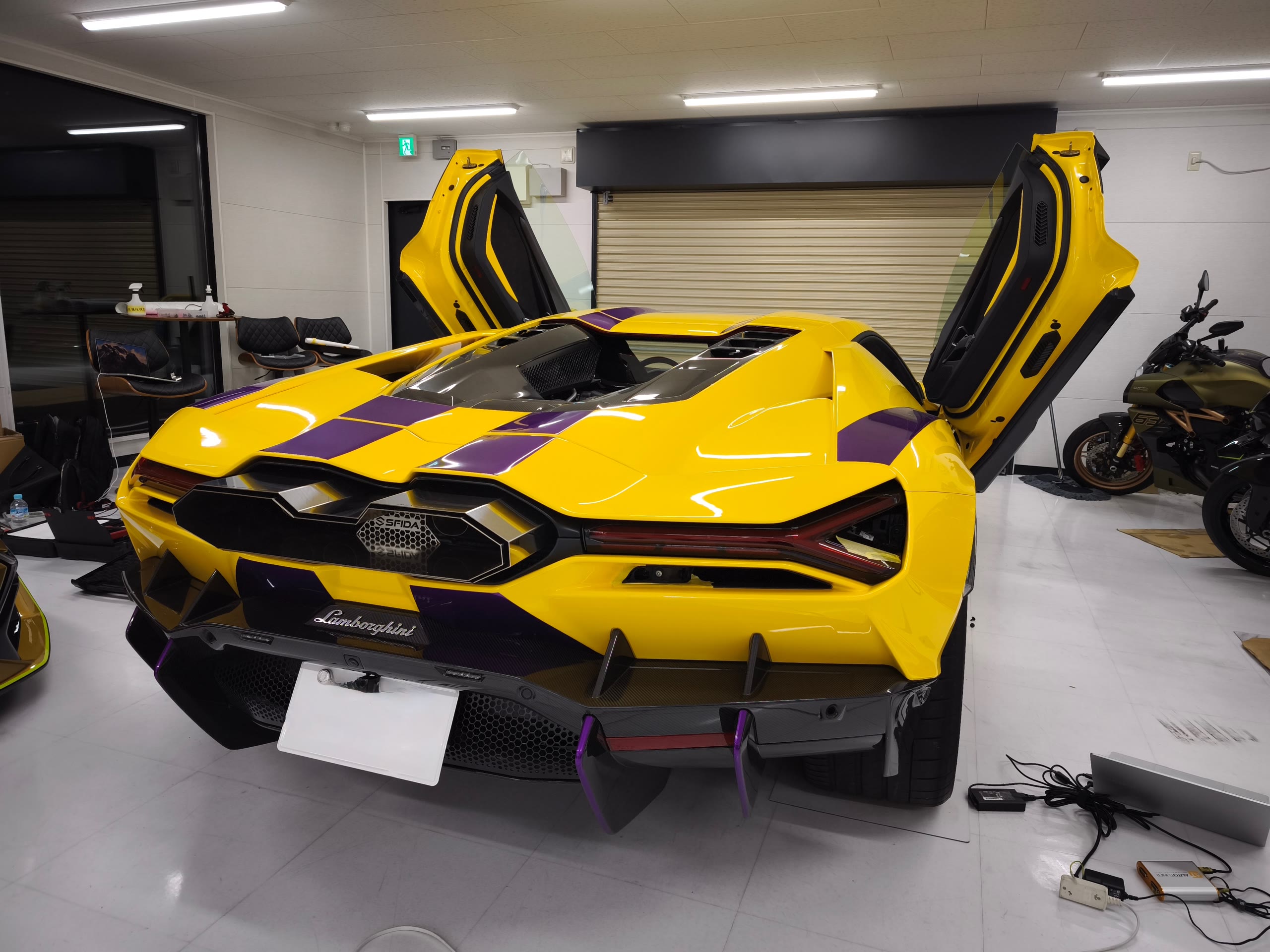 ワークショップ内でシザードアを開けた黄色×紫のランボルギーニ レヴェルトのリアビュー