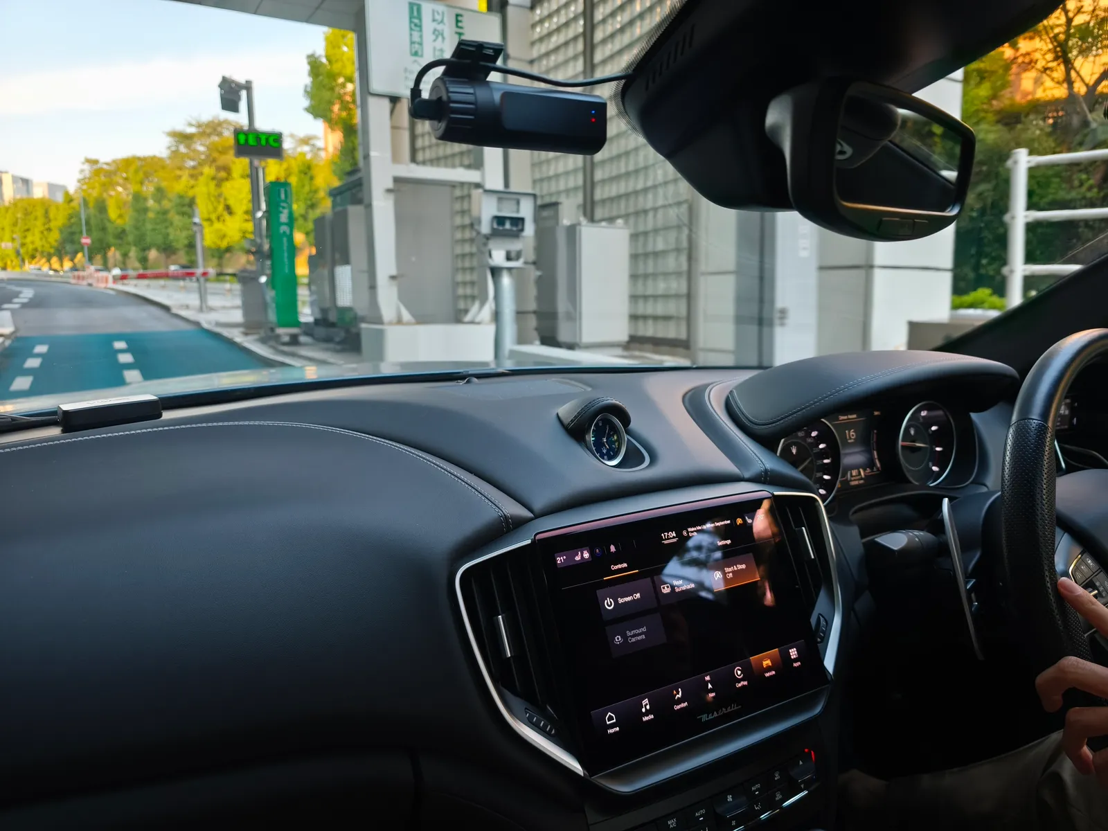 Driver’s-eye view of a modern car interior with a large touchscreen infotainment screen, steering wheel, and dashboard; street scene visible through the windshield.