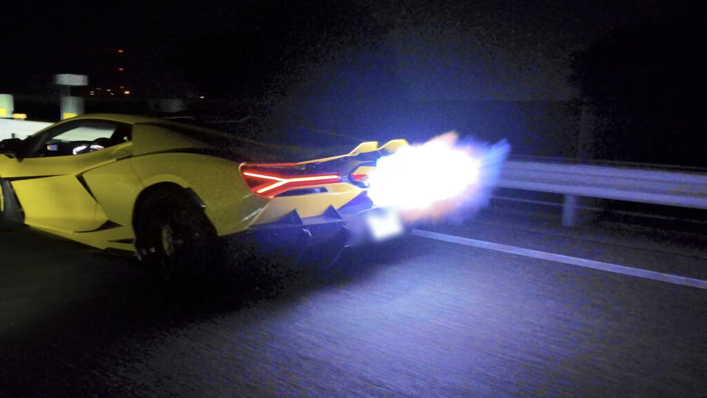 revuelto-map-switch-afterfire-flames – mbFAST Tuning Yellow sports car on a dark highway with its rear end damaged and bright flames spewing from the exhaust at night by a guardrail
