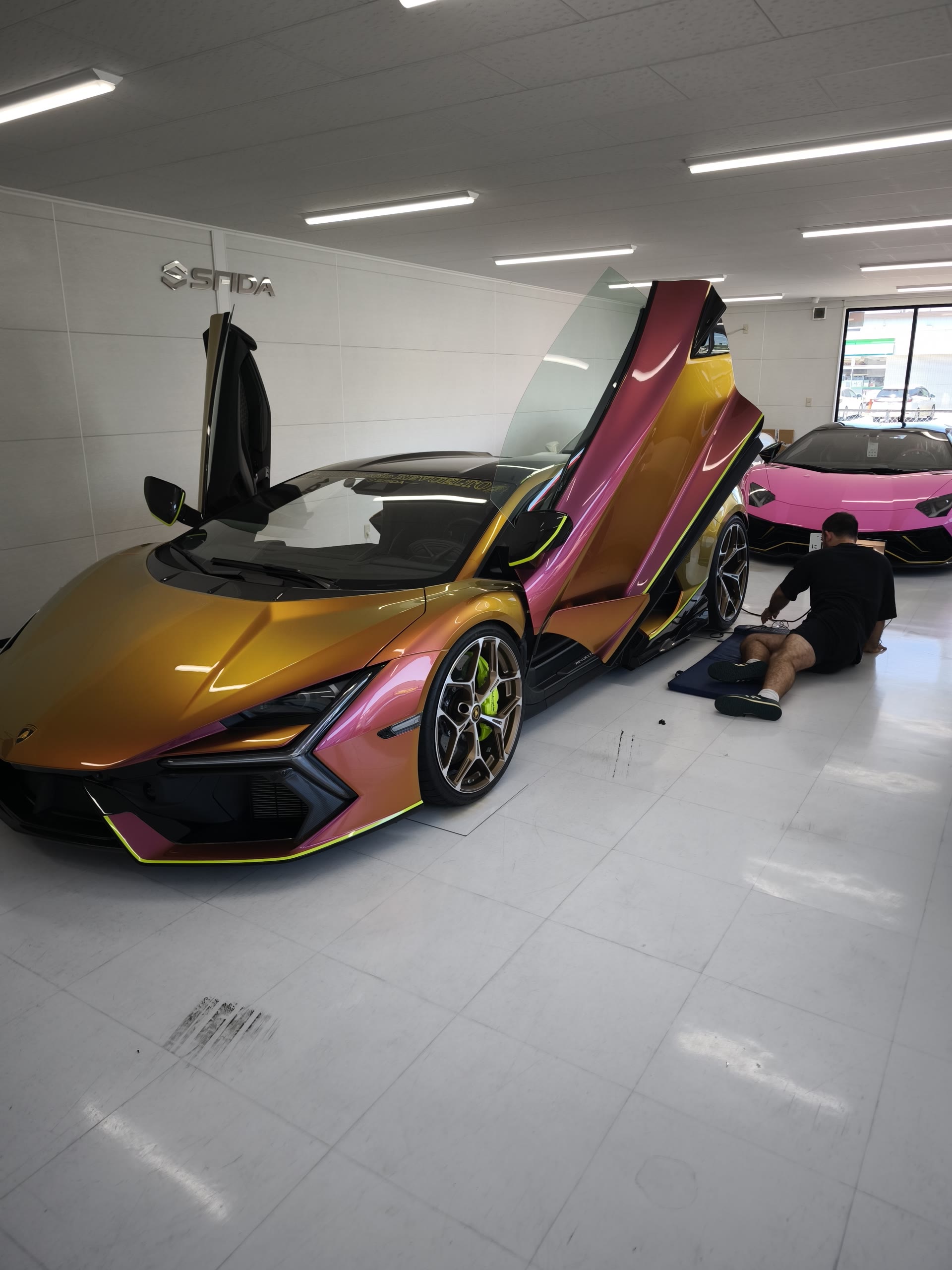 SFIDAショールームでドアを開けたマジョーラカラーのランボルギーニ レヴェルト。奥にピンクのアヴェンタドール