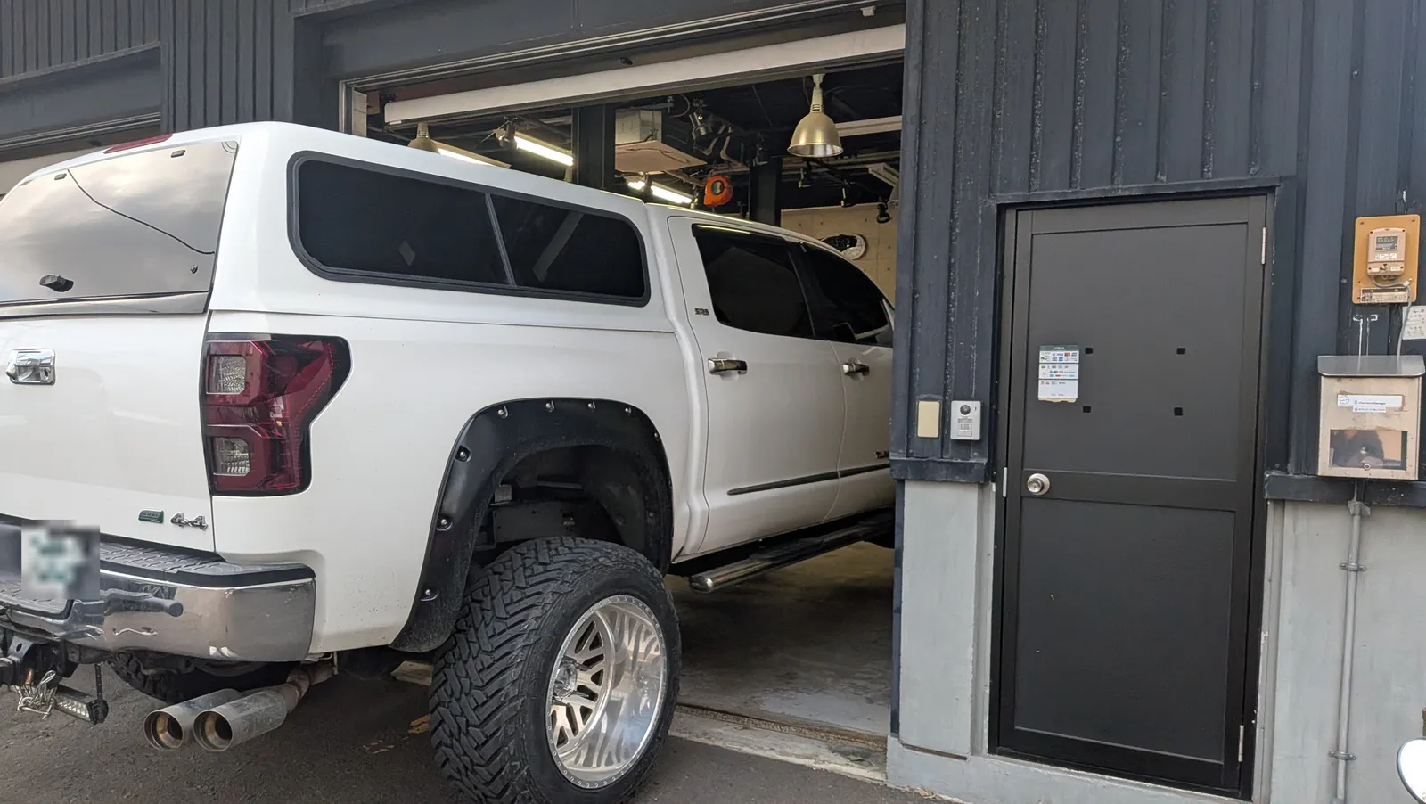 tundra-bubbling-tune-3 – mbFAST Tuning White pickup truck with oversized off-road tires inside a garage bay beside a dark gray door