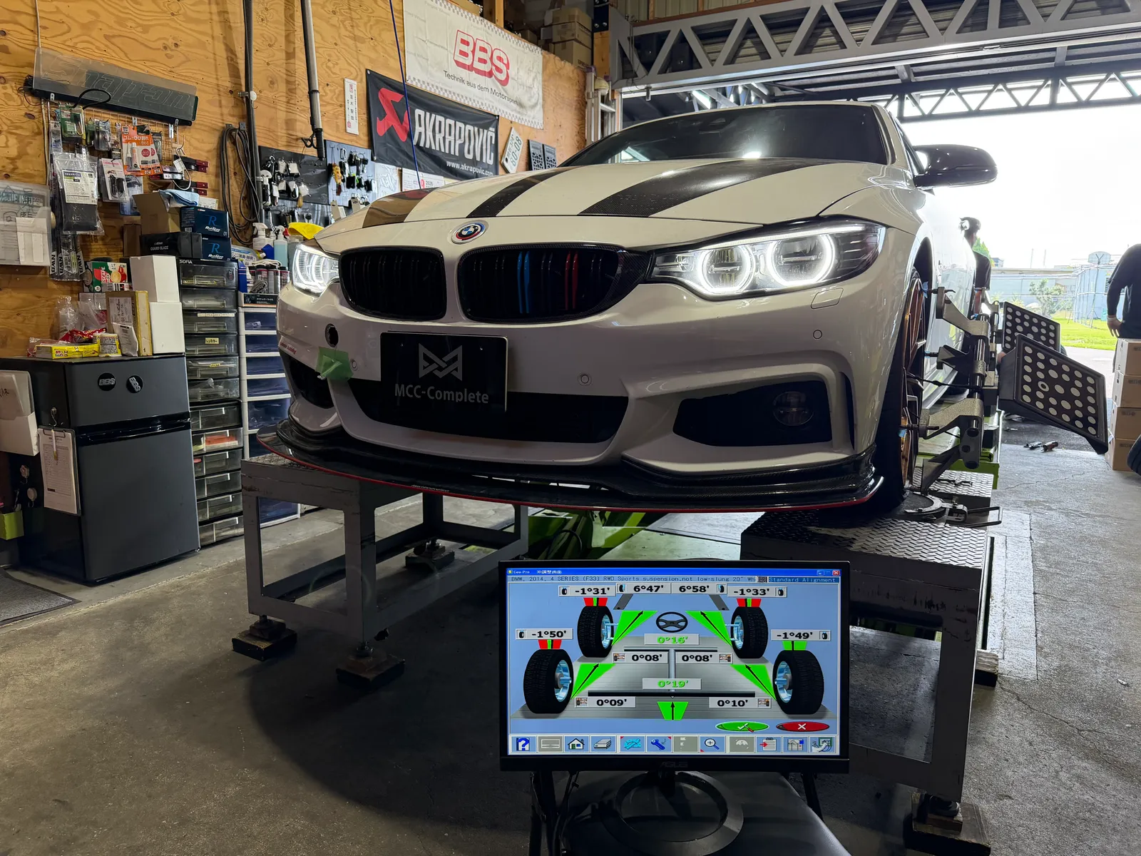435i-drive-shaft-replacement-1 – mbFAST Tuning White BMW on a wheel-alignment dyno in a workshop, monitor showing alignment data in the foreground.
