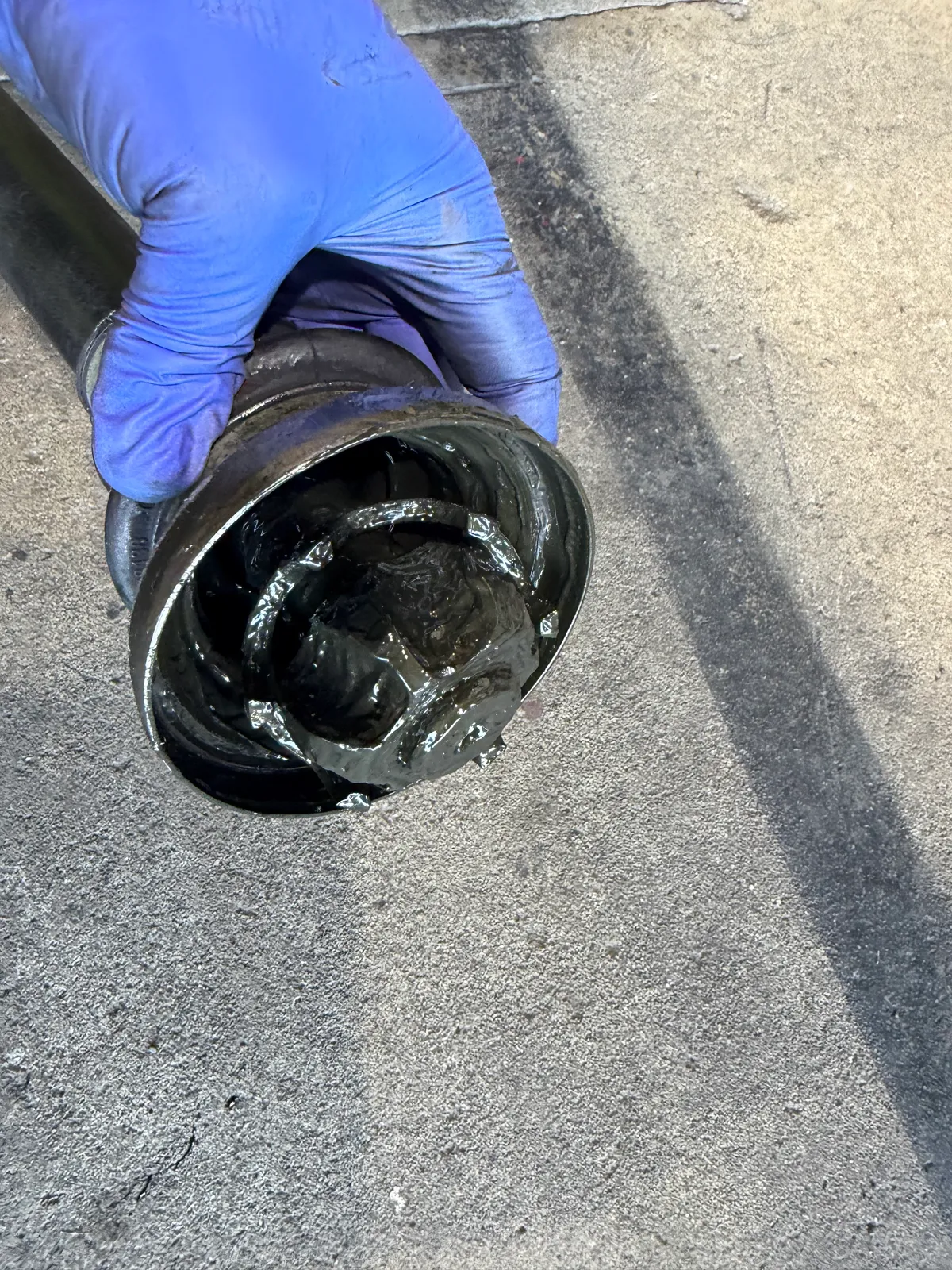 Gloved hand grips a thick, grease-covered cylindrical seal or gasket with black oil dripping.