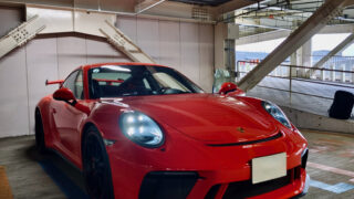 Red Porsche sports car parked in an indoor parking garage with exposed ceiling pipes above it.