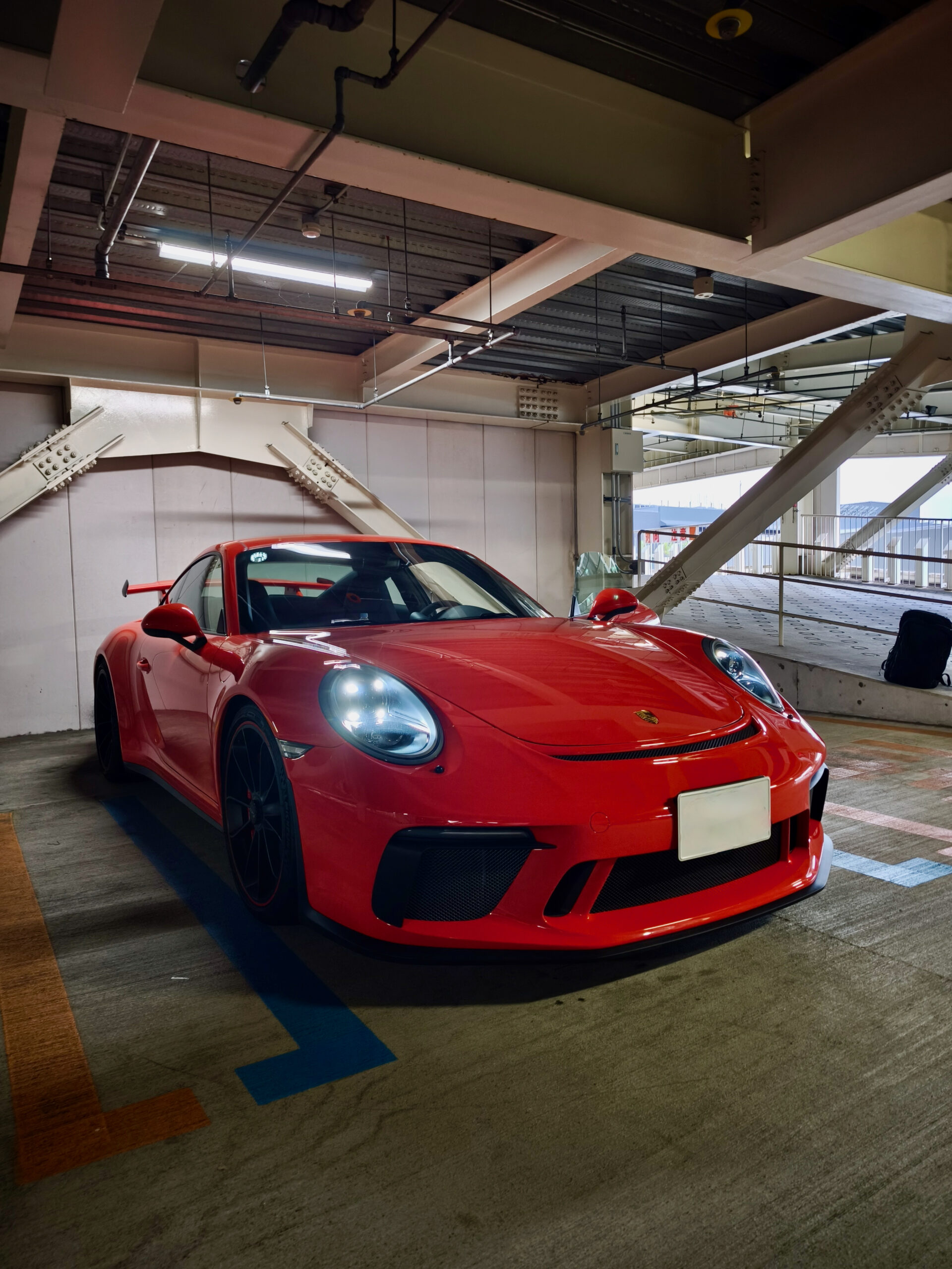 ポルシェ 991 GT3 ECUチューニング+バブリング施工車両 – mbFAST Tuning Red Porsche sports car parked in an indoor parking garage with exposed ceiling pipes above it.
