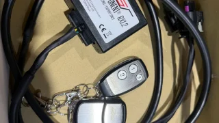 Automotive wiring kit with a small black control module labeled 'Component RX2', thick cables, and a two-key fob in a box.