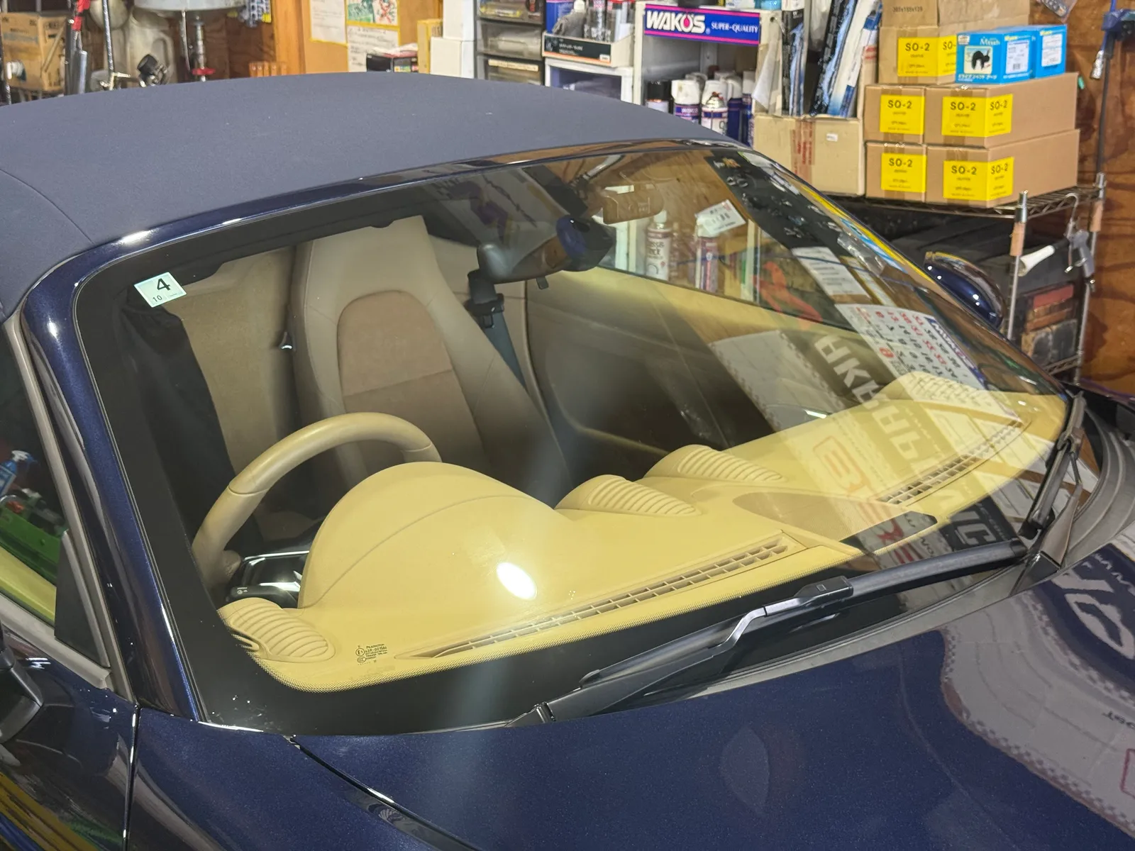 boxster718s-protection-film-4 – mbFAST Tuning Blue convertible with beige interior, parked in a cluttered garage visible through the windshield.