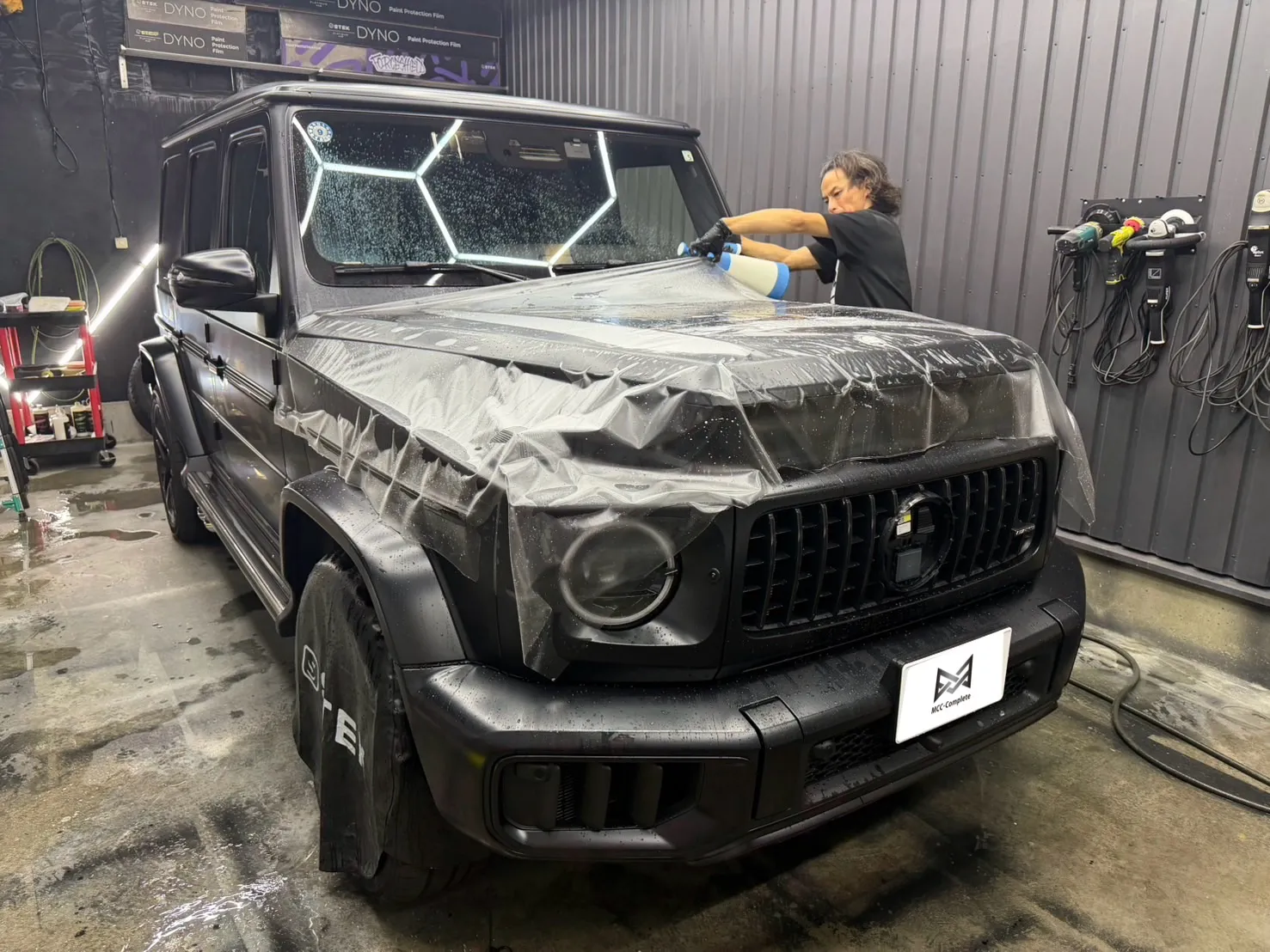 g63-w465-coating-polish-1 – mbFAST Tuning マット塗装のW465 G63 AMGのボンネットに施工者が保護フィルムを施しながら拭き上げている様子