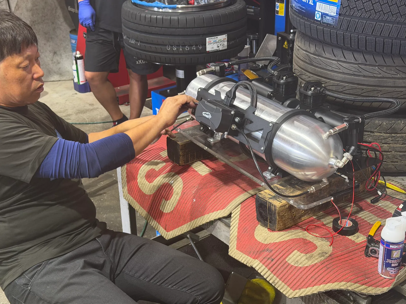 gtr35-air-suspension-3 – mbFAST Tuning Mechanic adjusting a compact pneumatic device mounted on a aluminum tank on a workbench with tires in the background