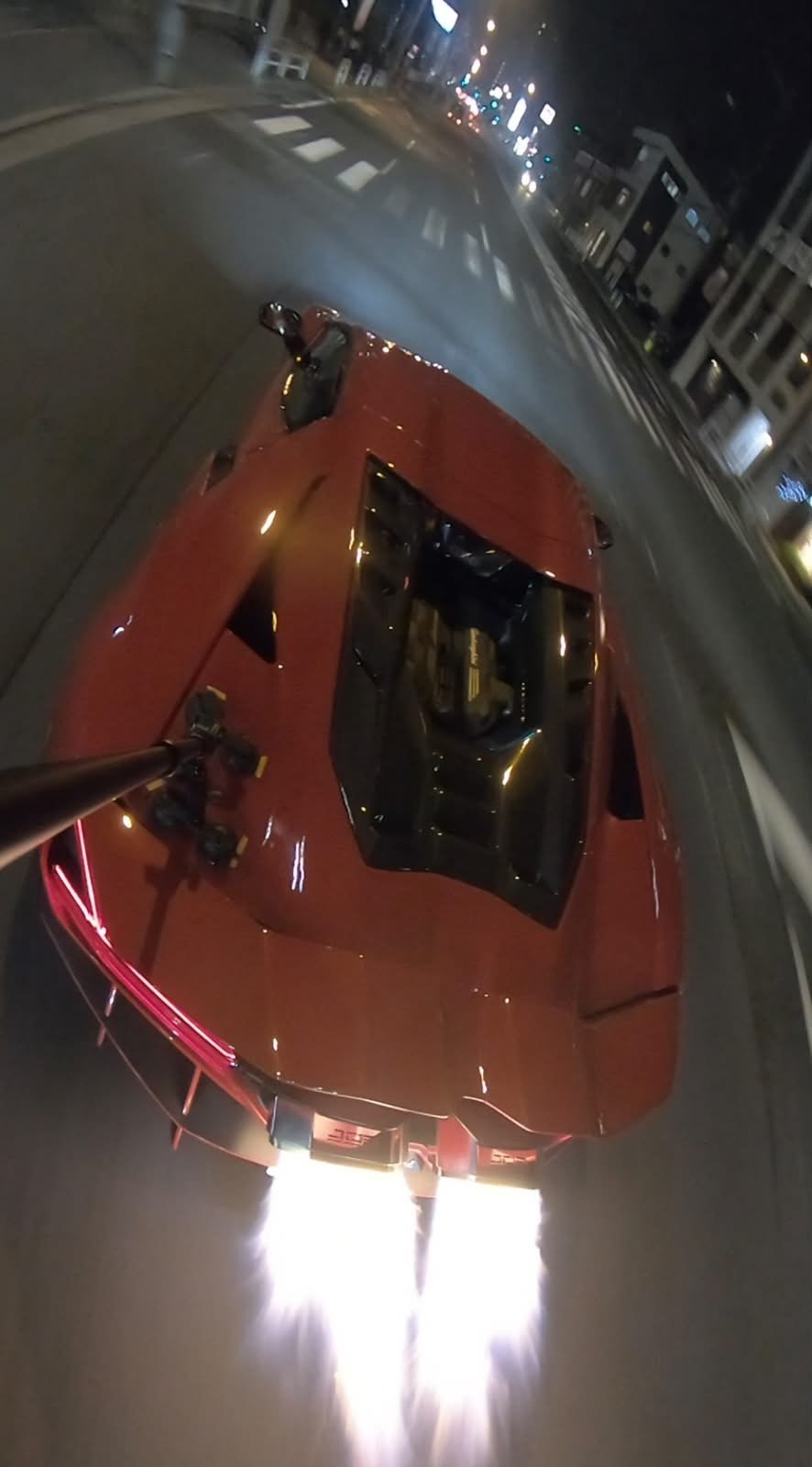 Red Lamborghini Revuelto at night on a city street, two long flames shooting from the exhaust tips on the overrun